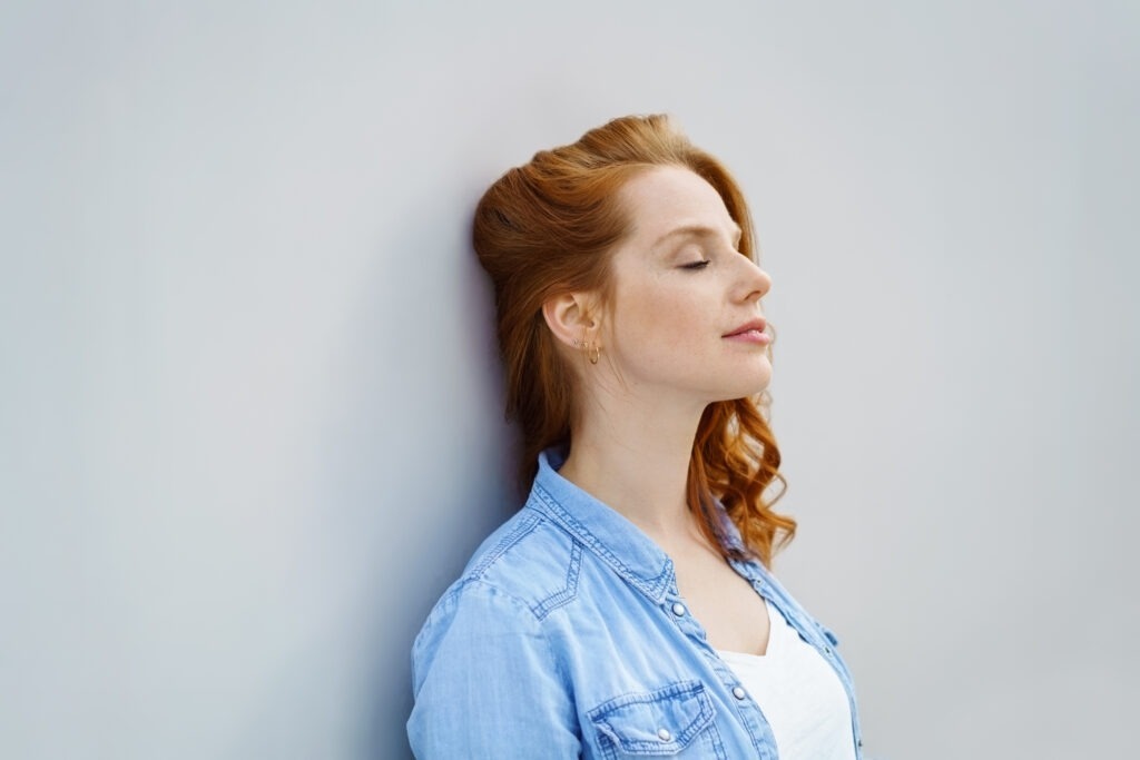 Femme apaisée, adossée à un mur, les yeux fermés, qui relâche la tension