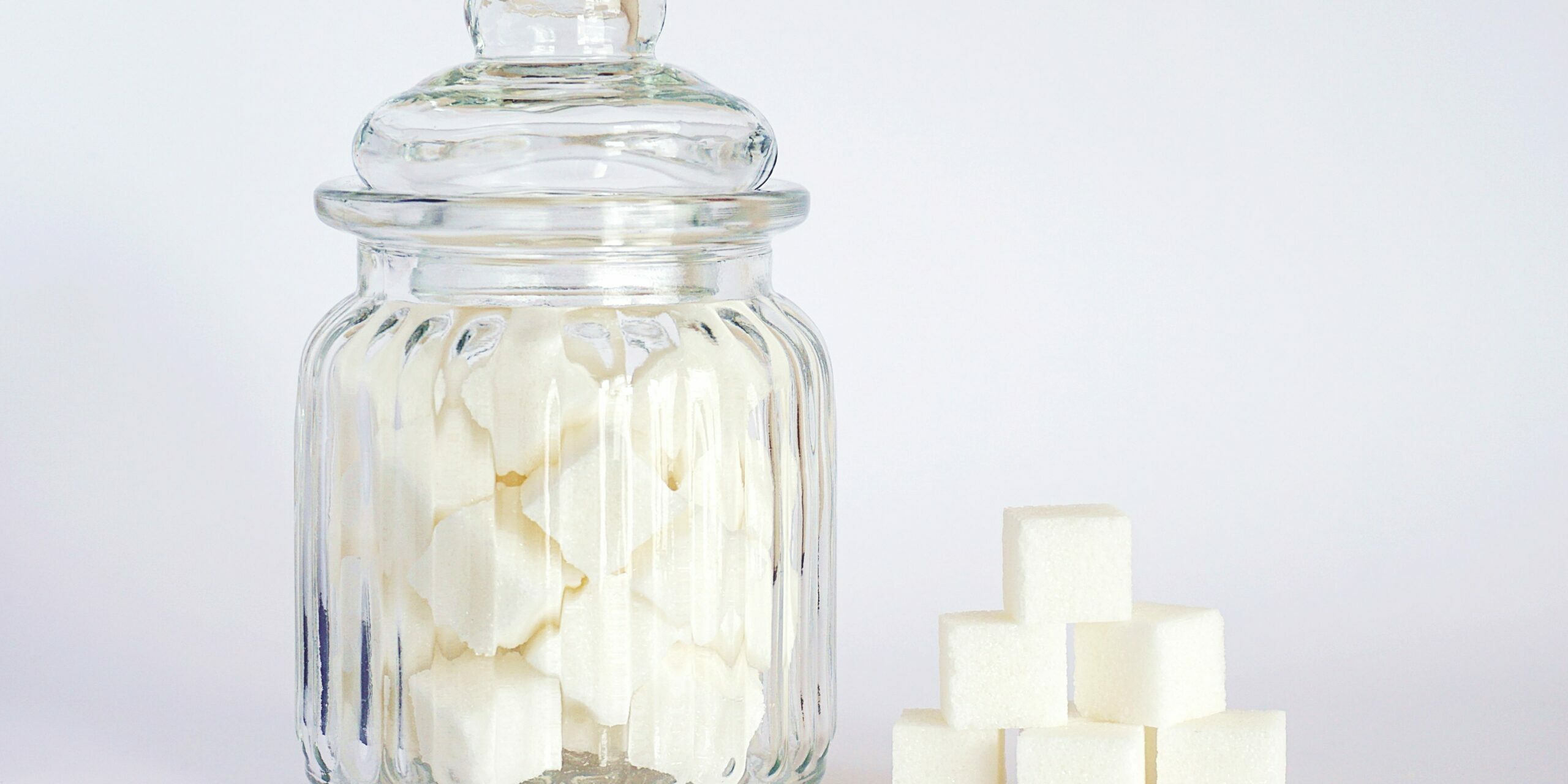 Addiction au sucre : comprendre le grignotage émotionnel Bocal en verre rempli de morceaux de sucre et cubes empilés, symbole de l’addiction au sucre et du grignotage émotionnel